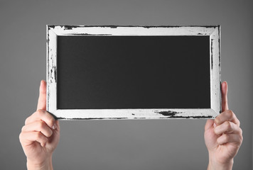 Female hands holding empty blackboard on color background