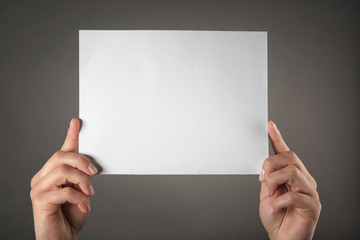Female hands holding empty paper sheet on color background