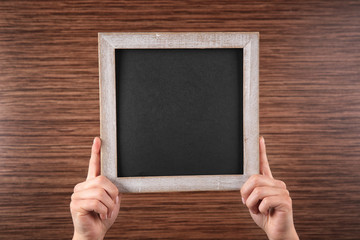 Female hands holding empty blackboard on wooden background
