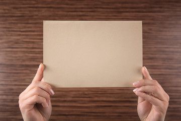 Obraz premium Female hands holding empty paper sheet on wooden background