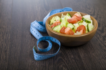 Salad in wooden bowl and measuring tape on a table close-up.
