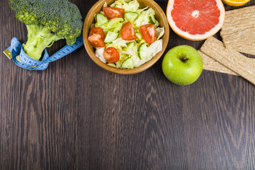 Food for diet and measuring tape on a dark wooden table.