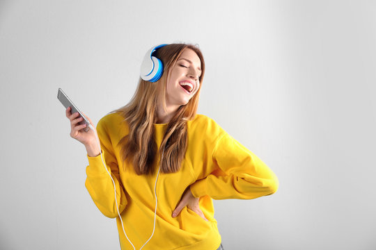 Beautiful young woman listening to music in headphones on color background