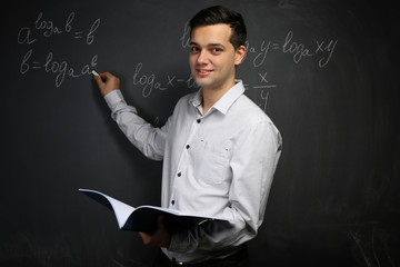 Handsome young teacher writing math formulas on blackboard