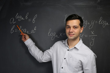 Handsome young teacher explaining math formulas written on blackboard