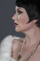 1920s style brunette dancer with short hair and jewelry. She is wearing a white hair shawl