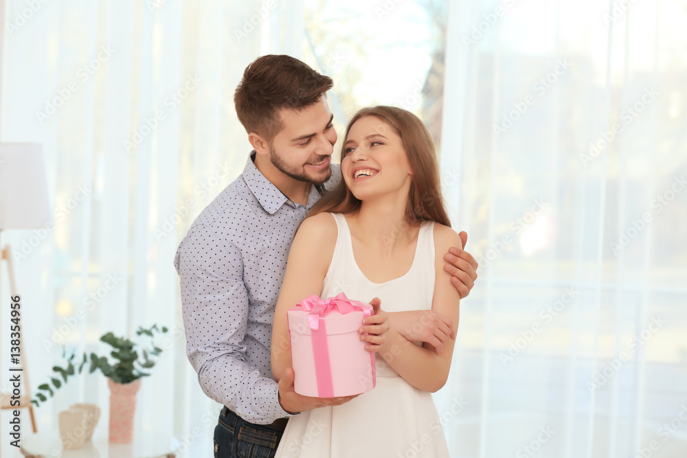 Poster handsome young man giving present to beautiful woman at home