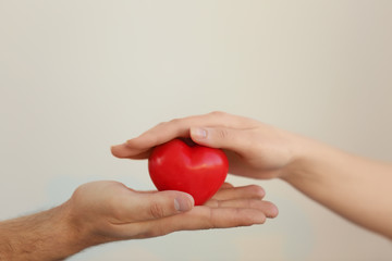 Obraz premium Male and female hands holding small red heart on light background
