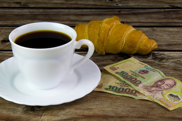 White cup of black coffee, croissant and Vietnamese money