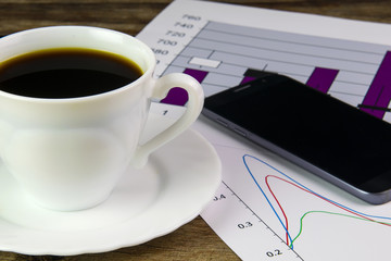 White cup of black coffee, graphics, phone and dollars
