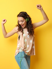 Beautiful young woman in headphones listening to music and dancing on yellow background