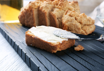 Tasty slice of beer bread with butter on wooden cutting board