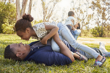 Parents Playing With Children On Grass In Summer Park