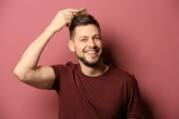 Fototapeta na wymiar Handsome young man combing hair on color background