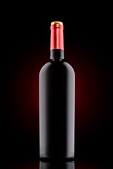 Red wine bottle at the black background with red spotlight