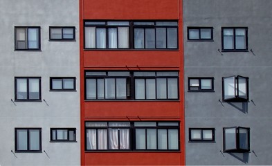 Front view of an apartment building facade colored with red, gray and light gray .   Windows pattern