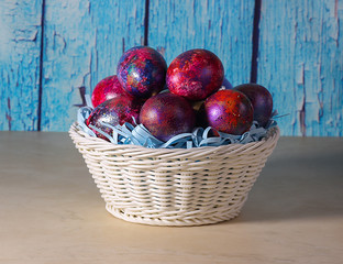White basket with colorful Easter eggs on a blue wooden background