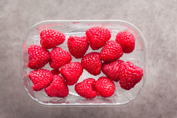 fresh ripe Raspberries in plastic container on gray