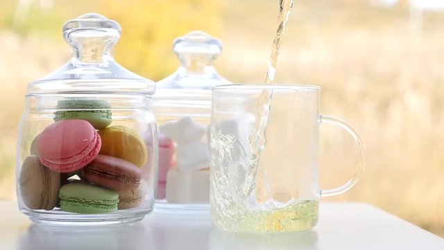 Cup of mint tea with macaroons and marshmallows. Beautiful sunny day in spring. Green and yellow background. French bakery with hot tea. Tasty breakfast, spring mood.