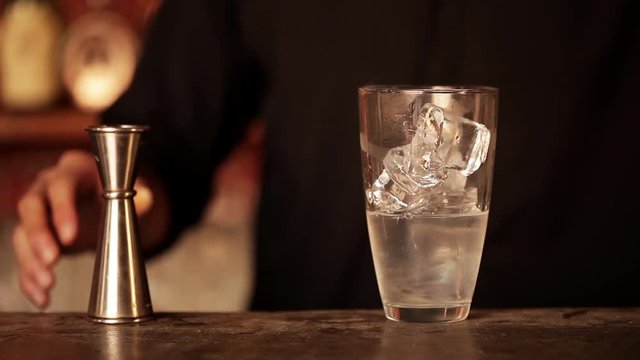 Bartender adding shot of cranberry juice to cocktail mixture in shaker
