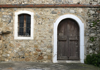 door and window with bar on a stone wall. Greece