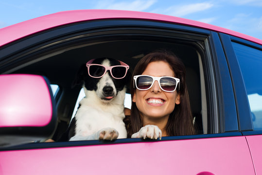Woman and dog in pink car on summer road trip vacation. Funny dog with sunglasses traveling. Travel with pet concept.