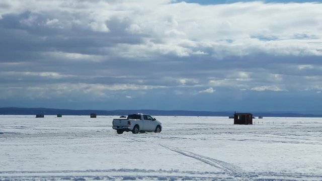 Pickup Truck Driving On A Frozen Lake In An Ice Fishing Camp,