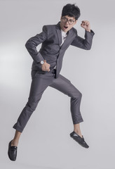 Fototapeta na wymiar Young handsome business man in gray suit and glasses jump because feel success with gray background