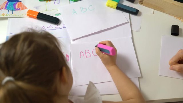 Happy family. Mother and daughter are learning to write. Adult woman teaches child the alphabet. Dolly shot.