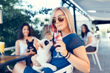 Beautiful young woman sitting in cafe with her adorable French bulldog puppy. Spring or summer city...