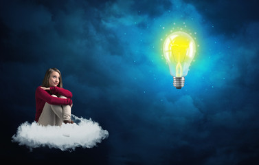 Fototapeta premium Woman sitting on a cloud lokking at huge lightbulb