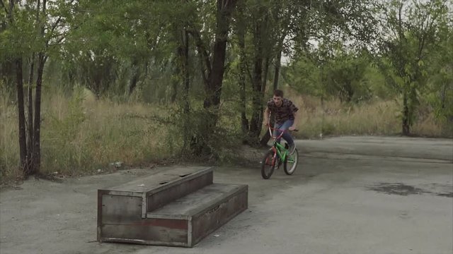 Ryder by special bicycle jumps through an obstacle and lands on a plain surface in the summer skatepark.