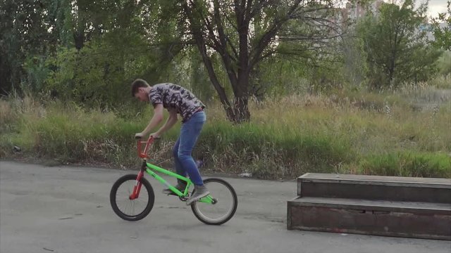 The guy jumps by bmx on the steps that are in the skate park, fulfills slip on the rear wheel, then jumps down on the asphalt, carrying the air around the scroll wheel frame