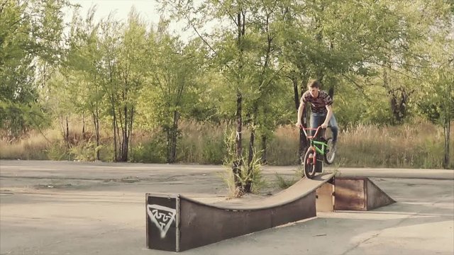 Ryder by special bicycle jumps through an obstacle and lands on a plain surface in the summer skatepark.