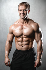 Brutal strong bodybuilder old man posing in studio grey background