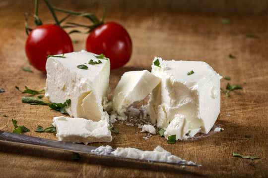 Feta cheese with knife and two cherry tomatoes in background on wood