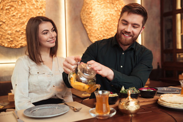 Cheerful young loving couple sitting in cafe and drinking tea.