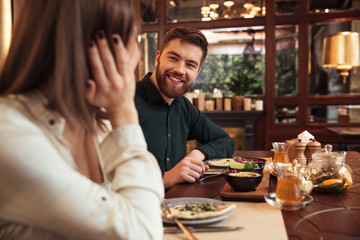 Cheerful young loving couple sitting in cafe and eating