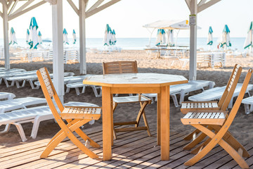 Wooden furniture in the restaurant on the beach, table and chairs made of solid wood on a background of sea and sun loungers