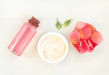 Skincare herbal cosmetics daily set, top view. Jar of cream, pink rose petals, facial tonic in...