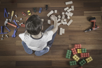 Little boy playing with toys. Kid sitting on the wooden floor in his room.Top view
