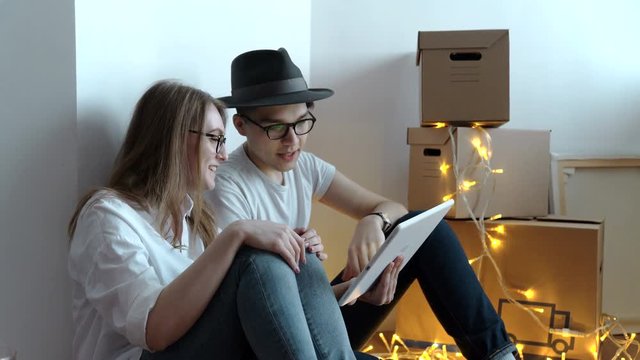 Young couple moving in new home.Sitting on floor and relaxing after cleaning and unpacking.Using tablet.