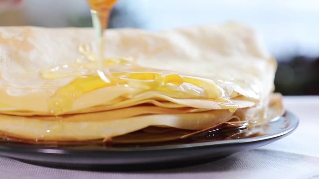 Honey is poured on a stack of pancakes. Sunlight. Close up. Slow motion.