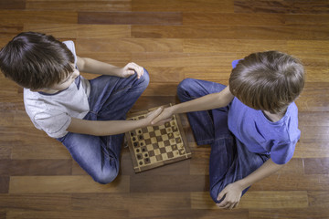 Kids shaking hands before game of chess sitting on wooden floor. Top view.