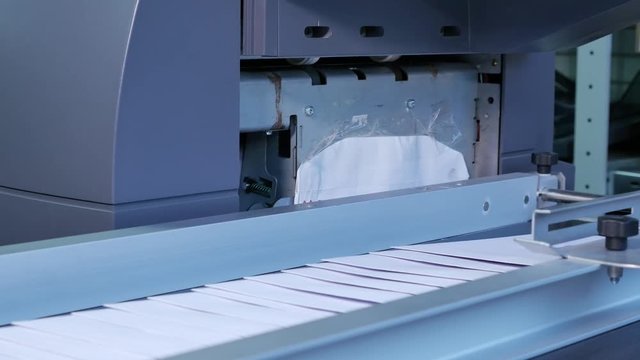 Passing white envelopes by machine in a factory, close up