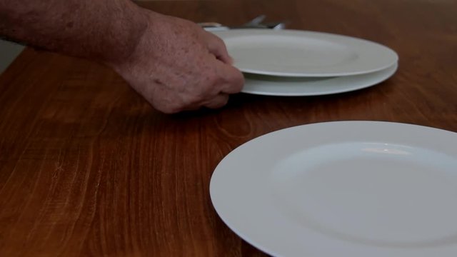 Male Hands Arranging Porcelain Plates and Tableware on a Brown Wooden Table