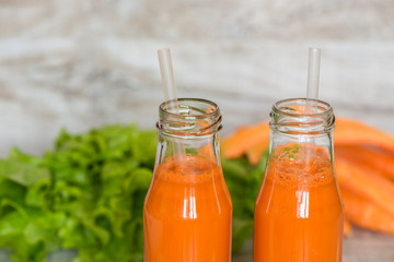 Fresh carrot juice in bottles on a grey wooden table