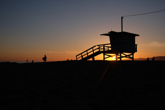 Silhouette of lifeguard tower and people on beach at sunset