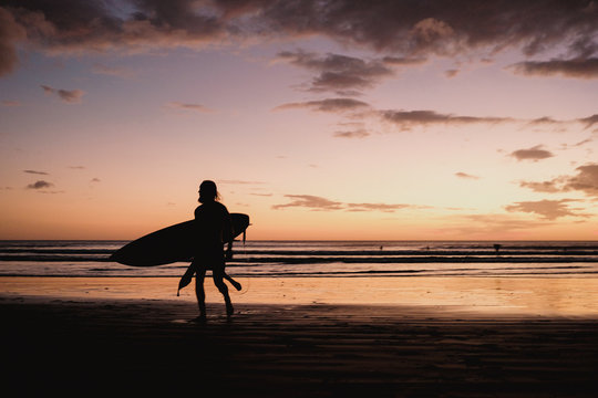 Silhouette of surfer carrying a surfboard on the beach at sunset