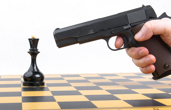 hand with gun took aim at chess piece